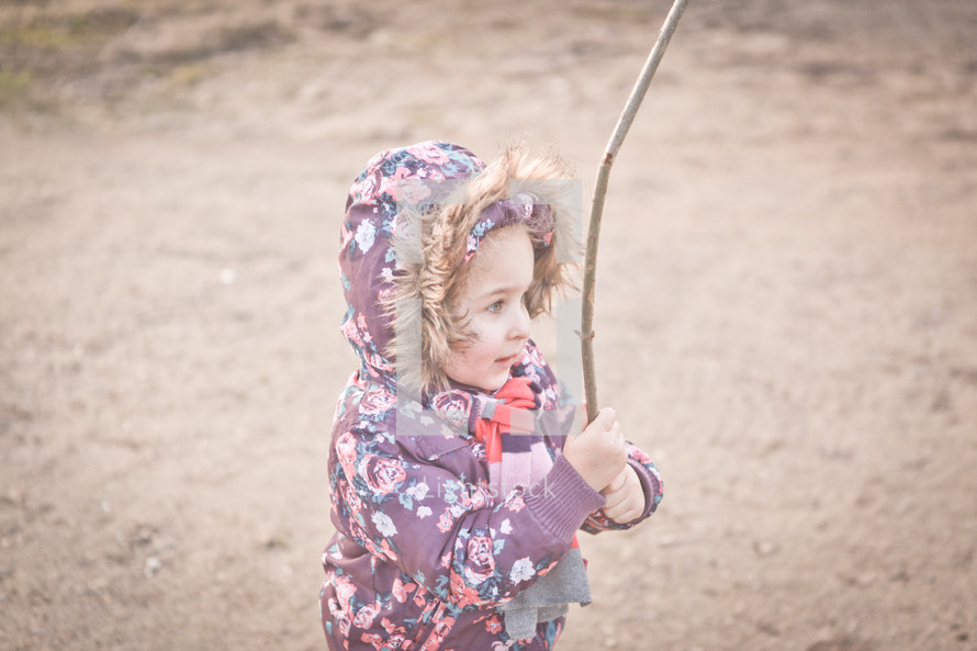 a girl child in a winter coat holding a stick outdoors 