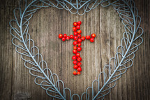 cross of berries in a blue metal heart on a wood background 