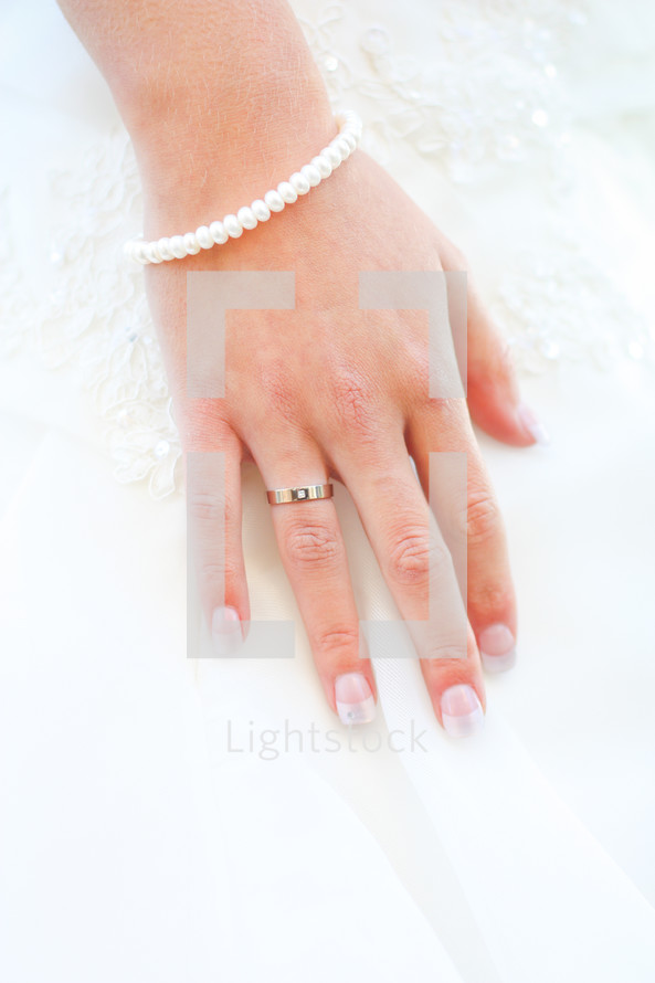 Bride's hand with wedding band and pearl bracelet.
