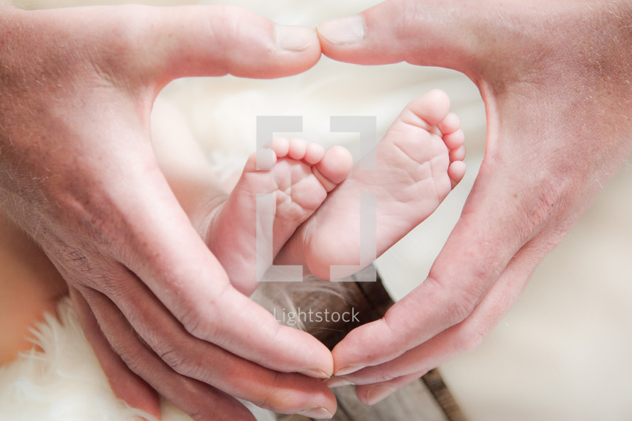 Infant feet surrounded by a father's hands.