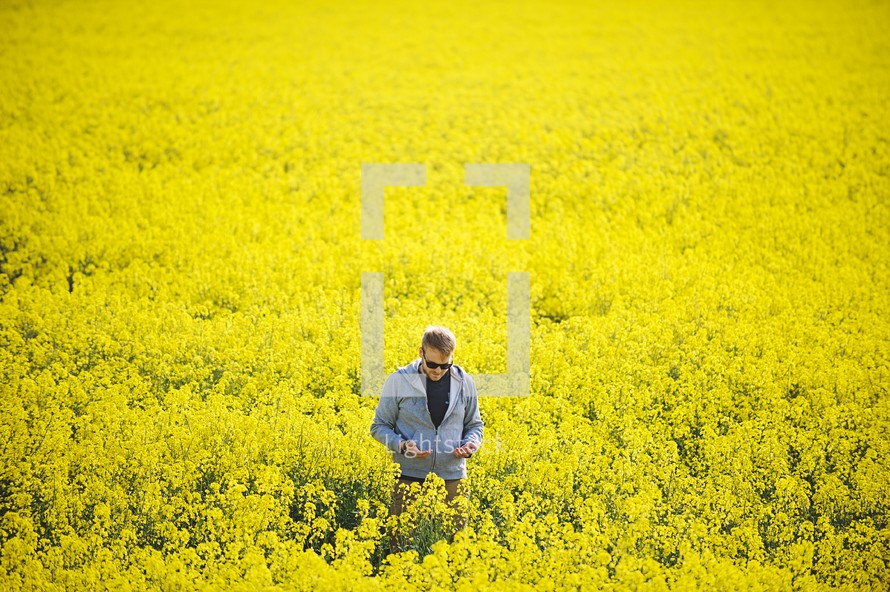 a man walking in a field of yellow canola flowers 