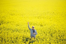 a man with his hand raised standing in a field of yellow flowers 