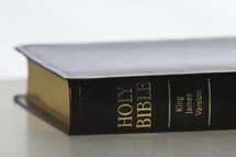 Spine of black and gold Bible laying on table.