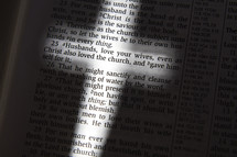 light glowing on the words of the pages of Bible in the shape of a cross