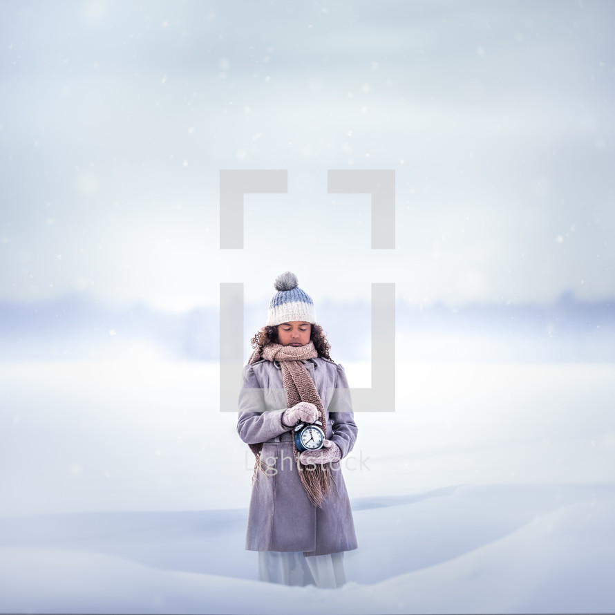 a girl standing in the snow holding an alarm clock 