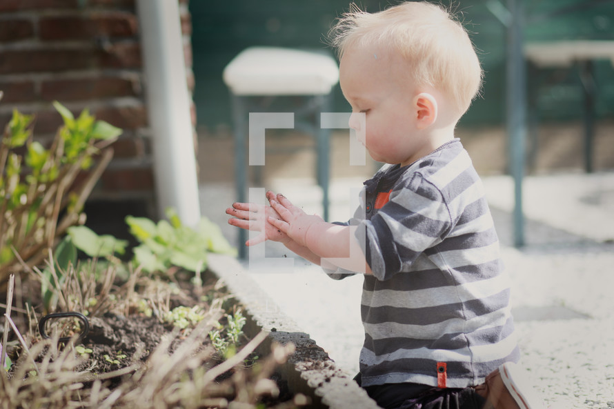 a toddler boy playing in dirt from a flower bed 