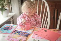 A little girl water coloring at the kitchen table.