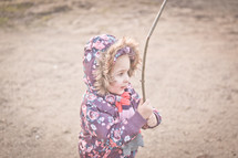 a girl child in a winter coat holding a stick outdoors 
