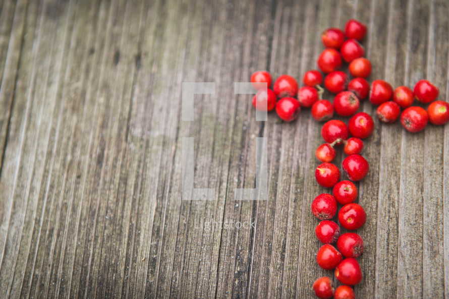 a cross of red berries on a wood background 