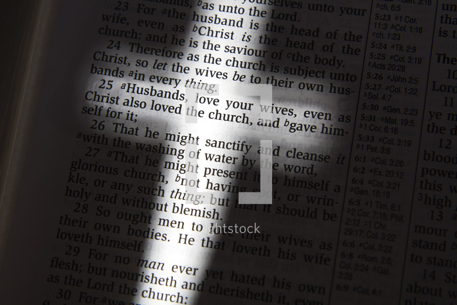 light glowing on the words of the pages of Bible in the shape of a cross