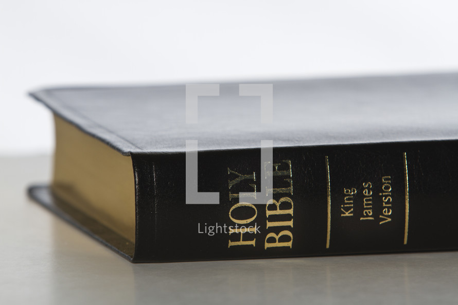 Spine of black and gold Bible laying on table.