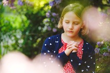 a girl standing under a flowering tree praying 