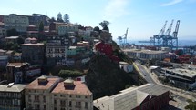 Aerial shot drone slowly approaches red house next to historical funicular next to large cranes on loading docks of coastal city on sunny day