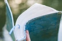 hand holding up a blue leather Bible outdoors 
