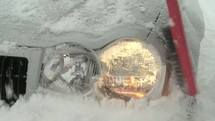 Cleaning snow off the headlight of a car.