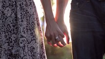 Couple holding hands outdoors at sunset.