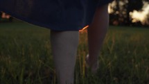 a girl walking through a field at sunset 