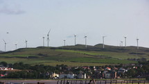 Moving wind turbines on a grassy hill over a town.
