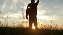 Silhouette of man in a field at sunrise jumping for joy. 