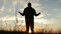 Silhouette of a reverent man praising God outside.