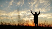 Silhouette of a man with lifted hands in worship outside.
