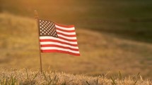 2 shots of an American flag in the grass waving in the breeze