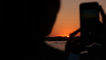 Woman taking a picture of the sunset on a beach.