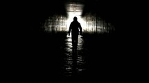 Silhouette of a man walking toward the light in a culvert, disappearing into the cross.