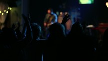 Silhouette of an audience with raised hands worshipping at a concert.