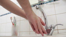 Washing hands with water at a sink faucet.