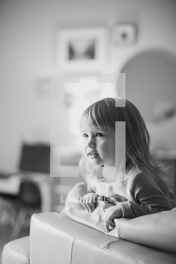 a toddler girl looking over a couch 