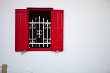window with wrought iron bars and red shutters