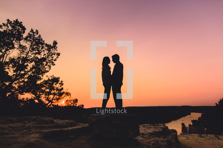 Couple standing on rock at sunset