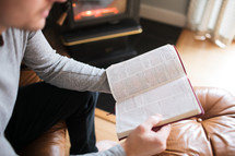 a man reading a Bible by a fireplace
