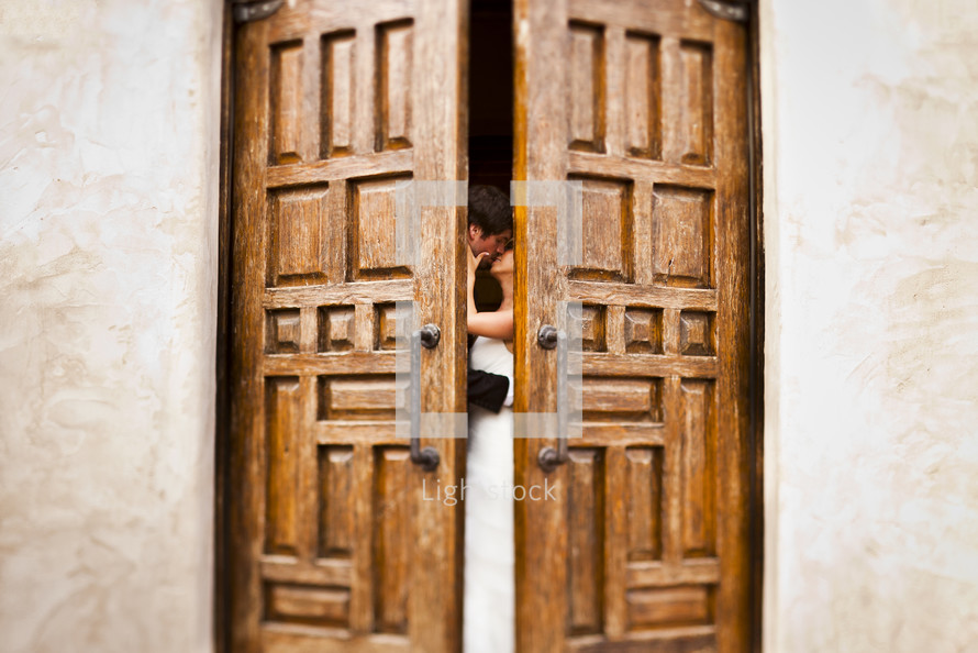 bride and groom kissing behind doors