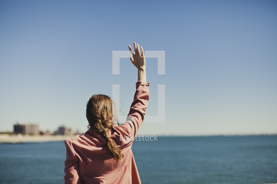 Woman raising arm gazing at ocean