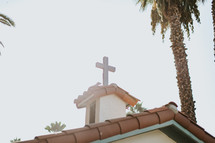 cross topper on the top of a church with a tile roof 