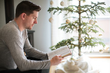 a man reading a Bible by a Christmas tree 