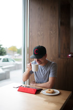 a man sitting in a window seating working at an iPad drinking coffee 