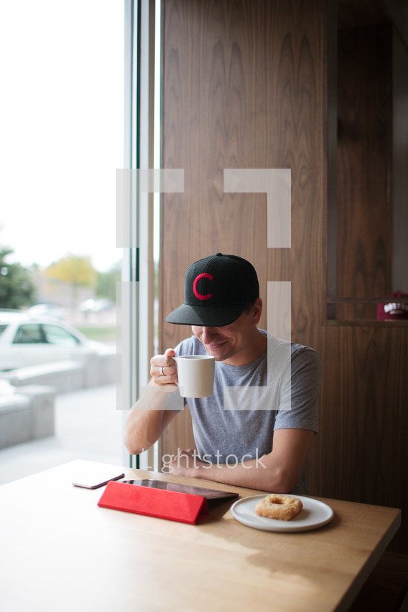 a man sitting in a window seating working at an iPad drinking coffee 