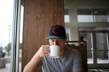 a man sitting in a window seat drinking coffee 