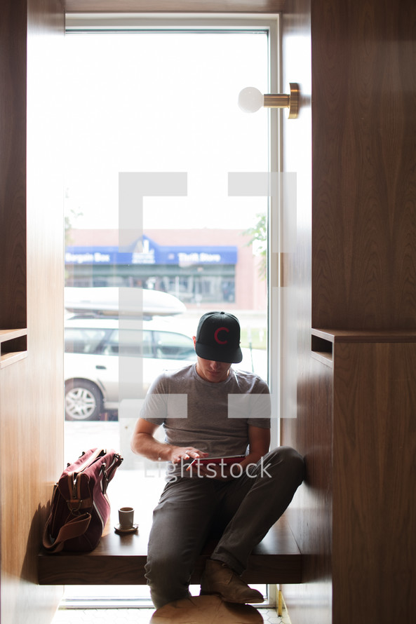 a man sitting in a window seating working at an iPad 