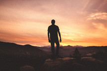 silhouette of a man standing at the top of a mountain