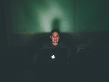 man looking at a laptop computer screen sitting in the dark 