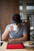 a man drinking coffee and looking at an iPad screen 