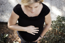 Pregnant woman with hands on her tummy outside.