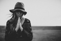 a woman with praying hands and a hat standing outdoors 
