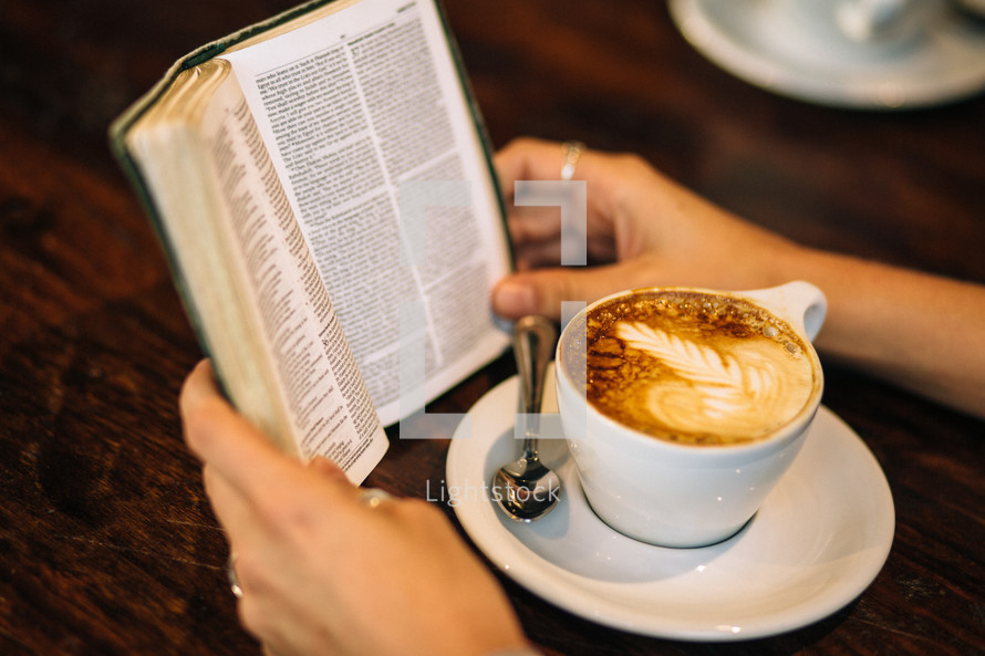 Hands on a wooden table with an open Bible and a cup of coffee.