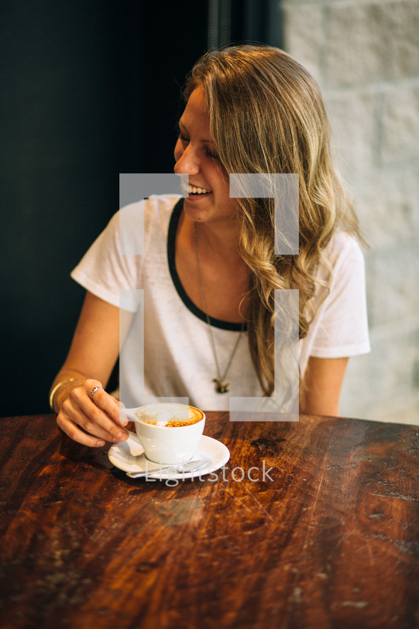 Smiling woman sitting at a table with a cup of coffee.