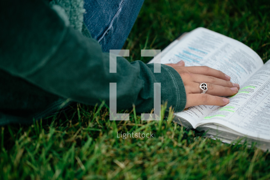 Hand on an open Bible in the grass.